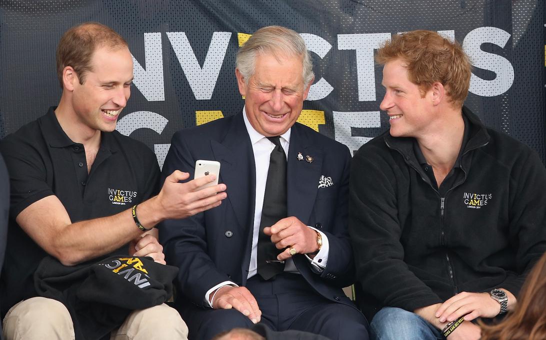 Принц Уильям в чёрной рубашке Invictus Games и бежевых брюках, Король Карл в чёрном костюме и галстуке, Принц Гарри в свитере Invictus Games и джинсах.