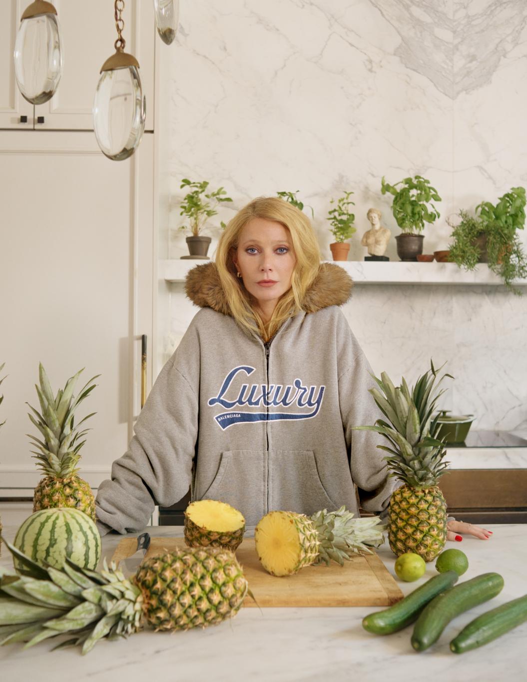 Гвинет Пэлтроу в худи Balenciaga «Luxury» у кухонной стойки с ананасами и другими фруктами.