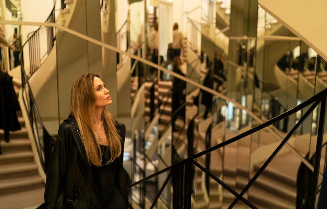 Анджелина Джоли смотрит вверх, стоя у зеркальной лестницы.