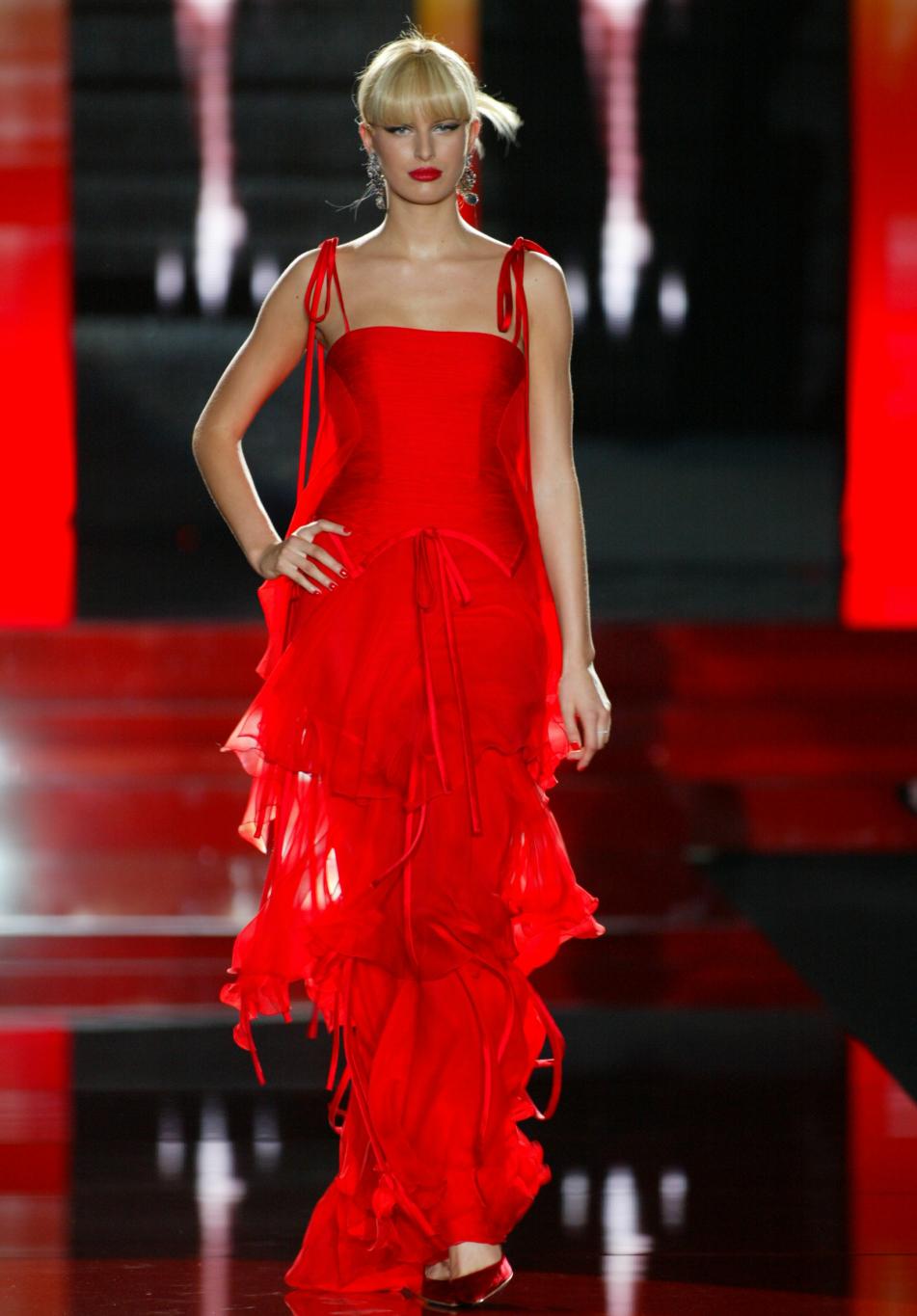 Модель в красном ярусном платье на тонких бретелях и красных балетках, на подиуме в красно-черном свете.