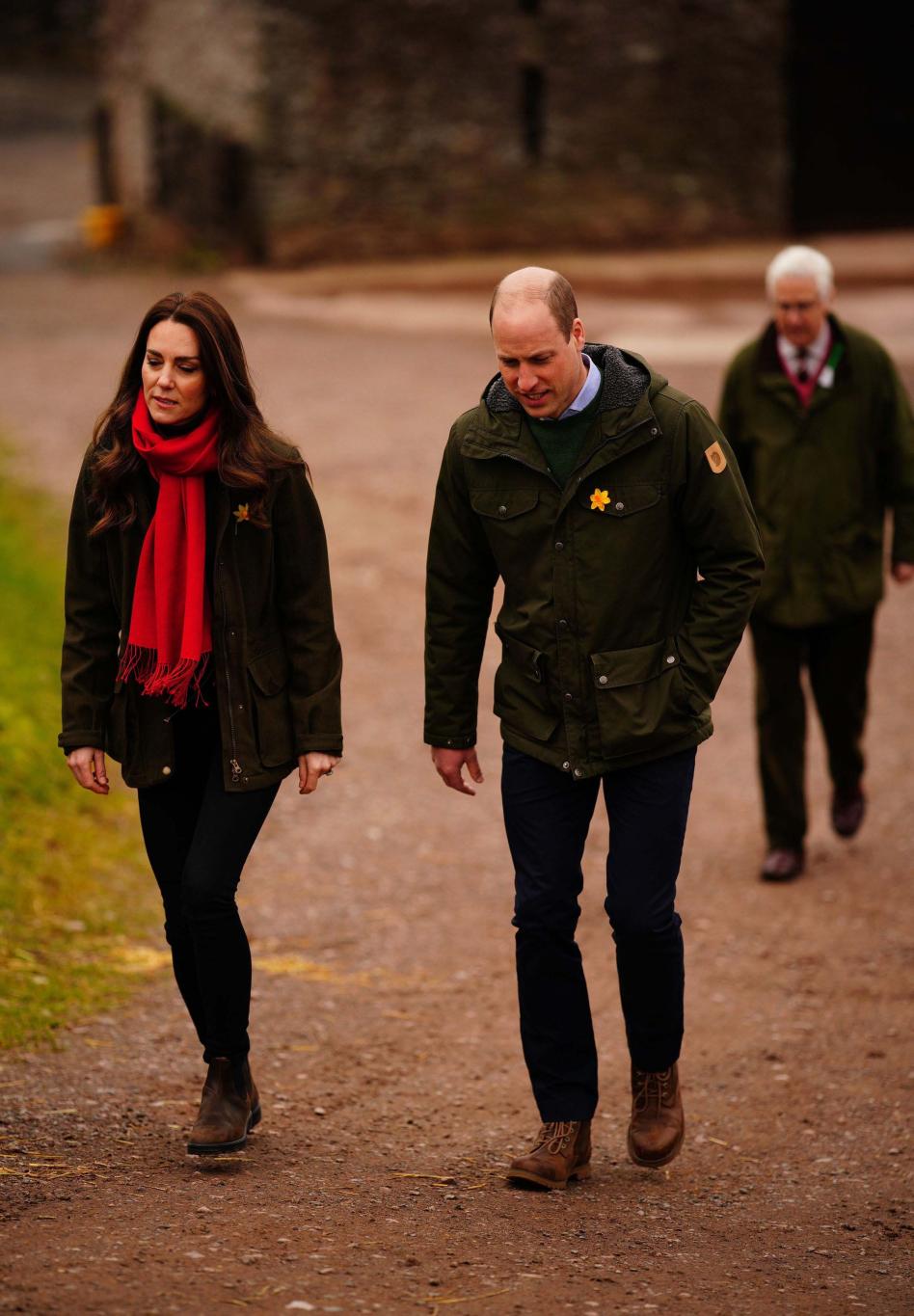 Принц Уильям и герцогиня Кэтрин прогуливаются по грунтовой тропе, за ними следует еще один человек.