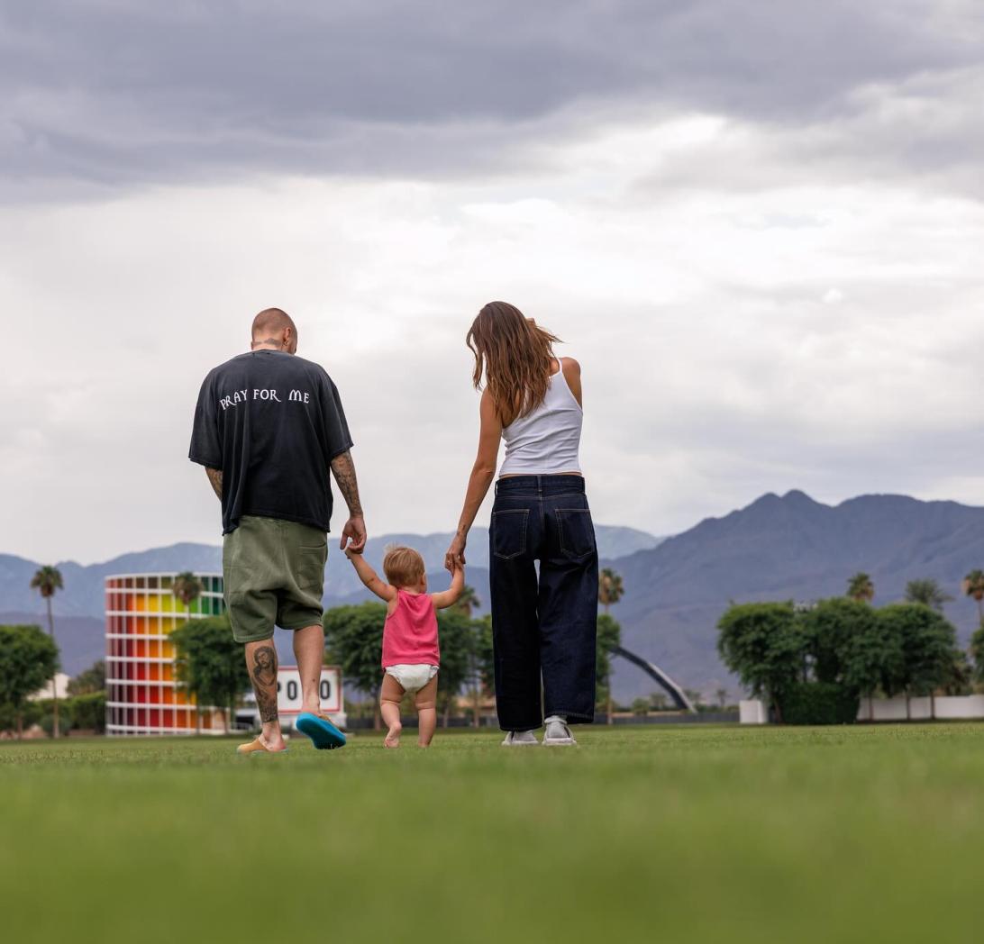 Джастин и Хейли Биберы с сыном Джеком Блюзом идут, держась за руки, по травянистому полю в Долине Коачелла.