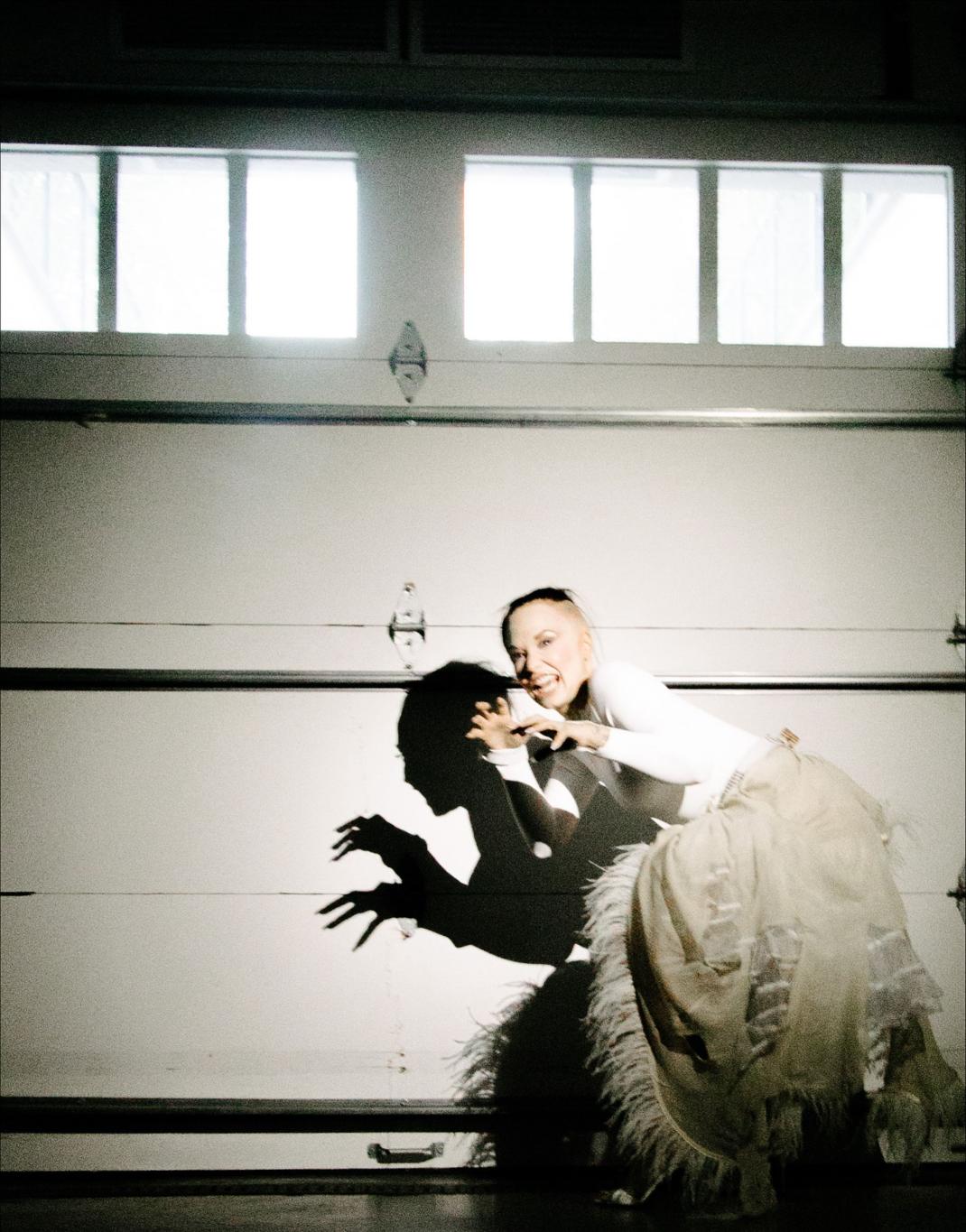 Деми Ловато в образе "Пут Ловато" в белом топе и многоярусной юбке, с темной тенью слева.