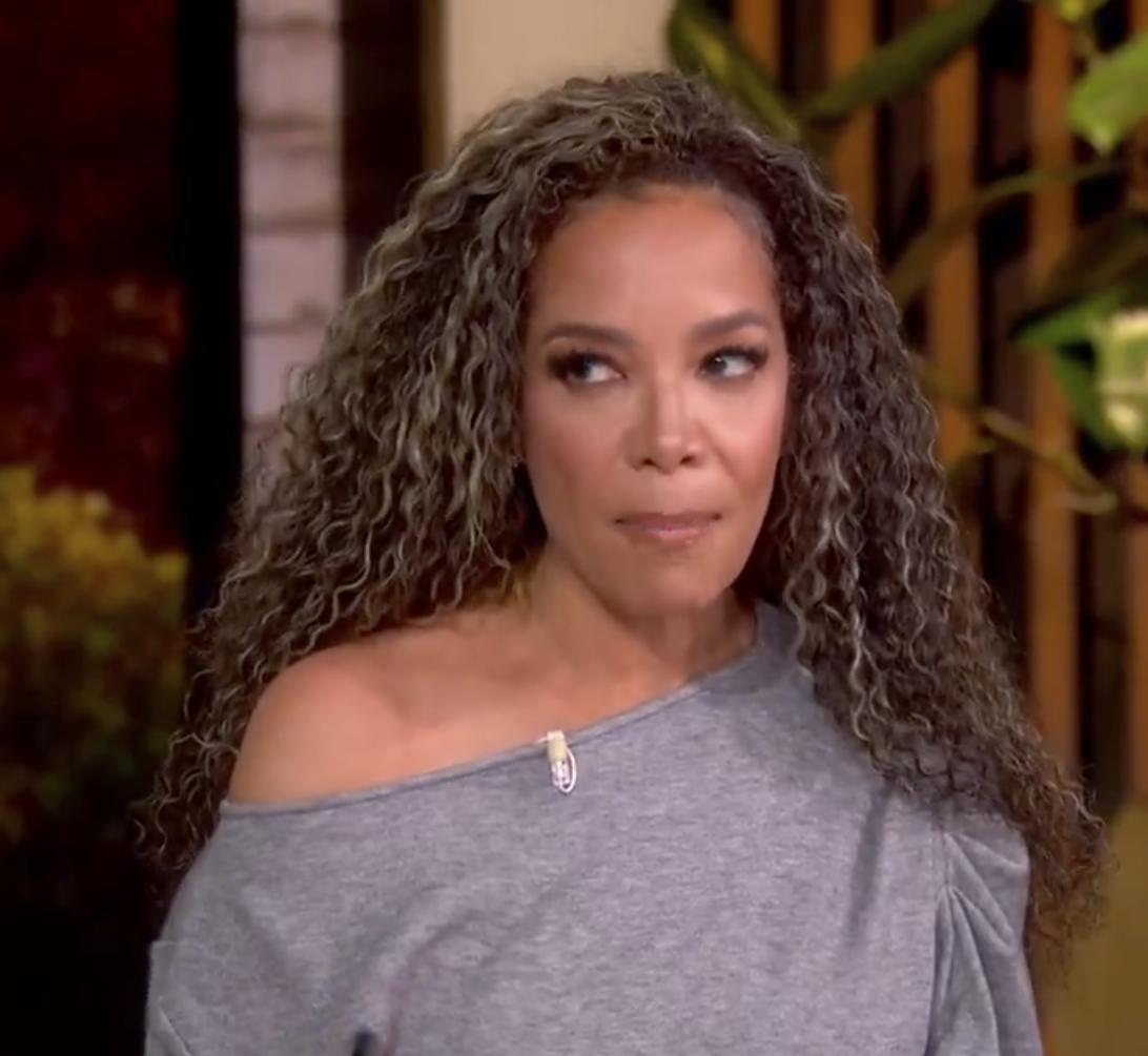 Вупи Голдберг в сером топе с открытыми плечами, смотрит вправо со слегка озабоченным выражением лица.