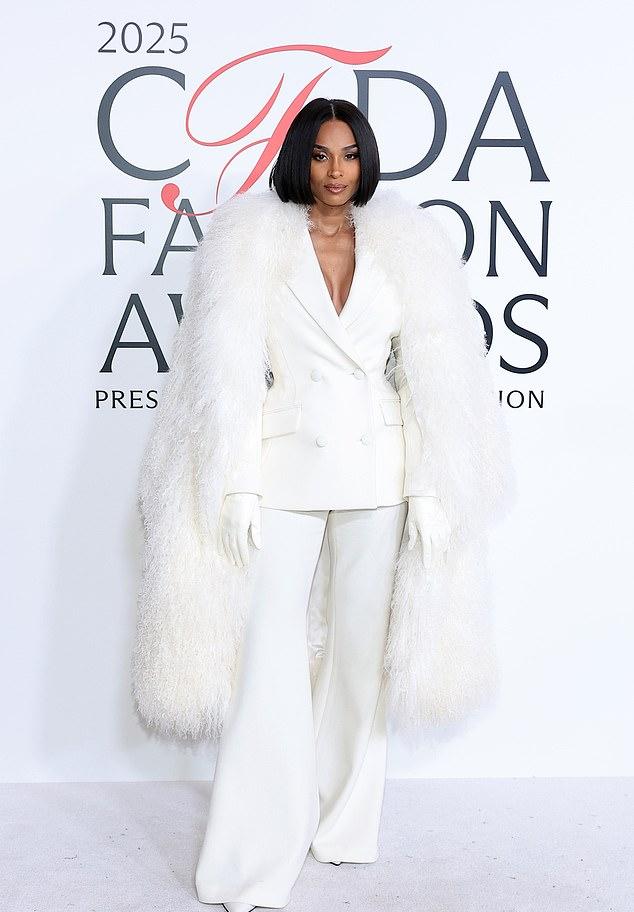 Сиара в белом двубортном костюме, подчеркивающим фигуру. Смелое декольте, брюки-клеш и пушистая накидка добавили шика.