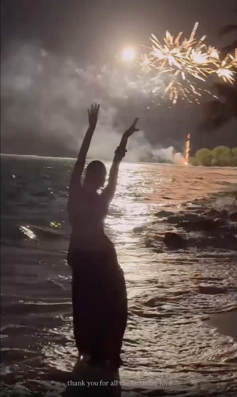 Силуэт человека в воде, освещенный взрывающимся салютом в ночном небе.