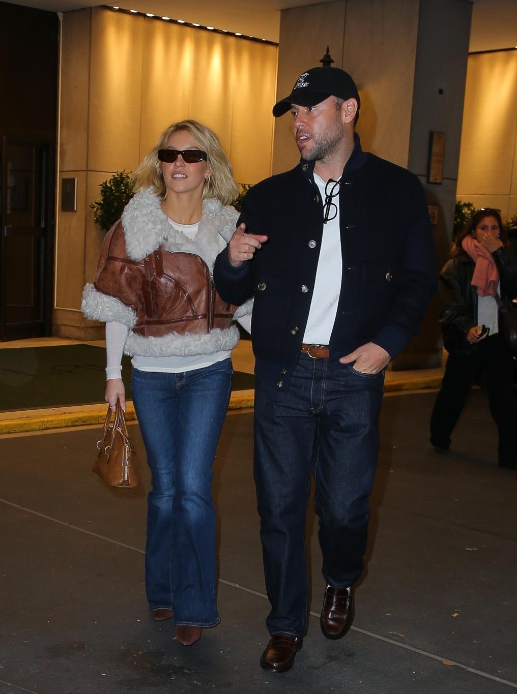 Сидни Суини в коричнево-белой дубленке, синих джинсах и очках рядом со Скутером Брауном в черном бомбере, темных джинсах и бейсболке.