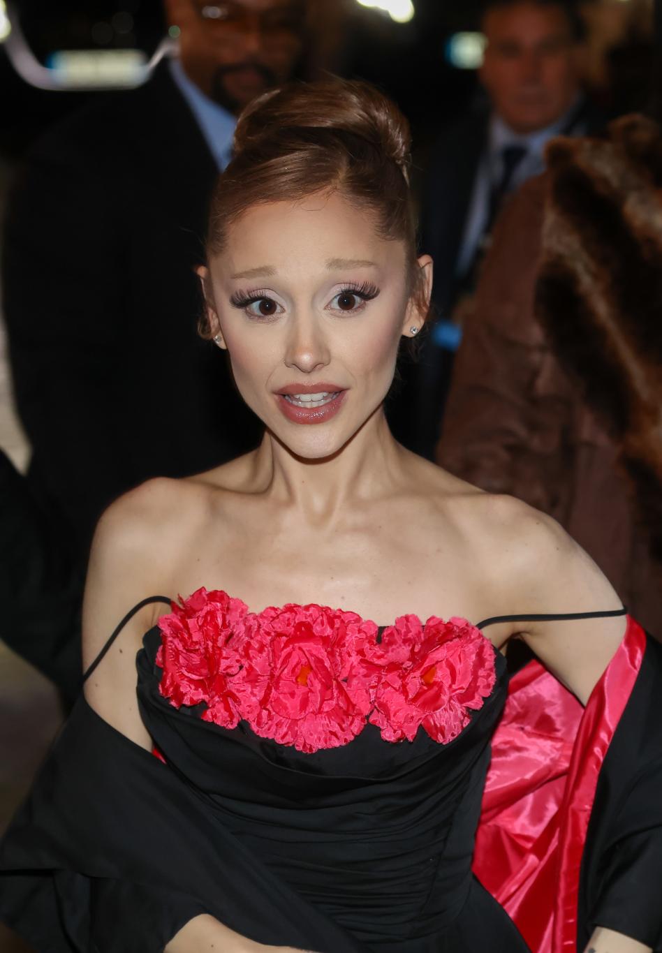 Ариана Гранде в черном платье с открытыми плечами и крупными розовыми цветочными аппликациями на лифе.