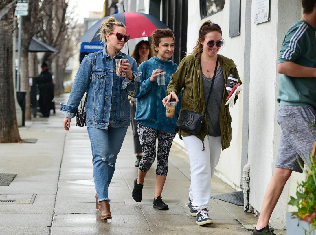 Сёстры Хилари и Хейли Дафф, в джинсовой и зелёной куртках, прогуливаются по улице с напитками.