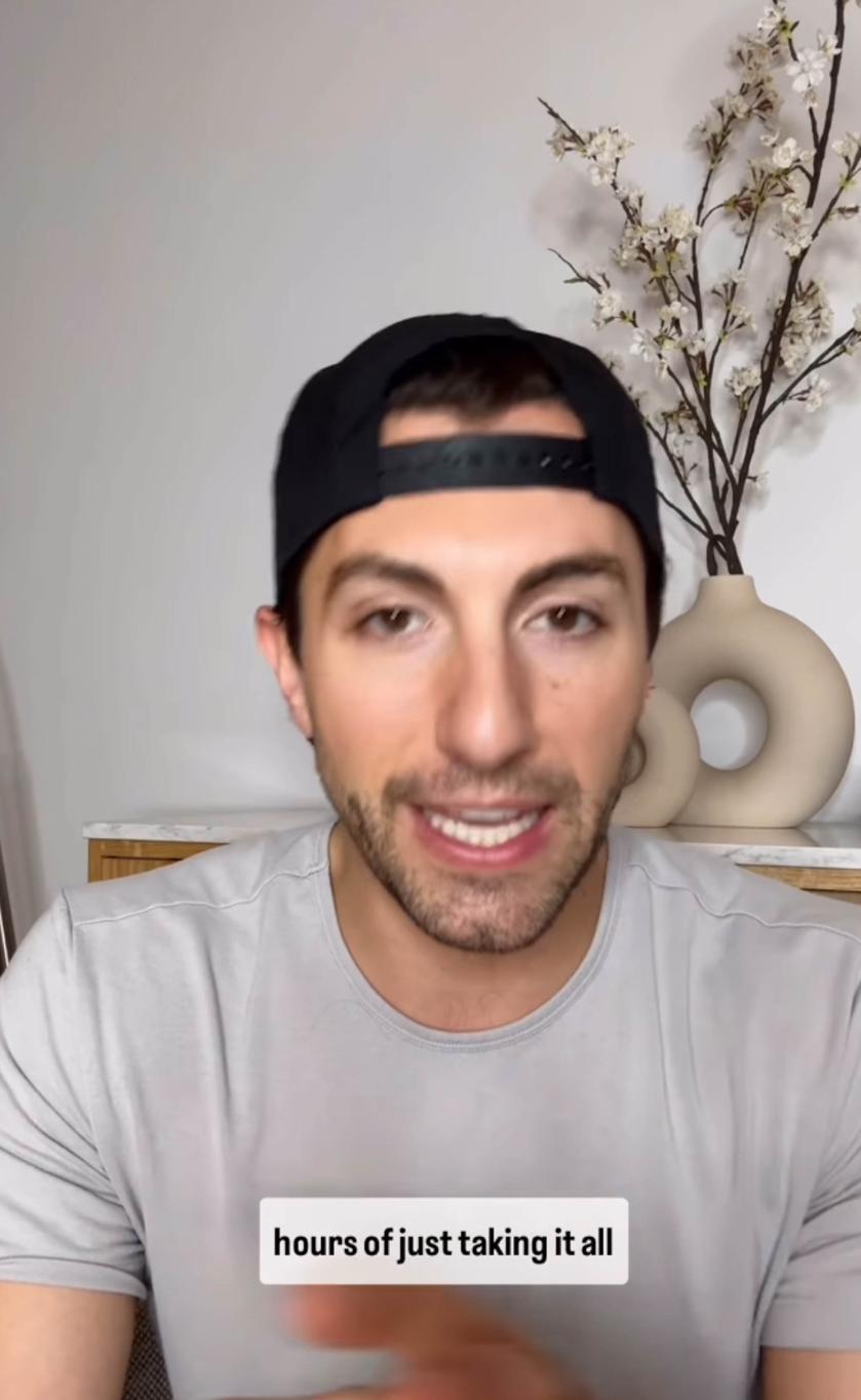 Мужчина в черной бейсболке говорит на фоне белых декоративных цветов в бежевой вазе.