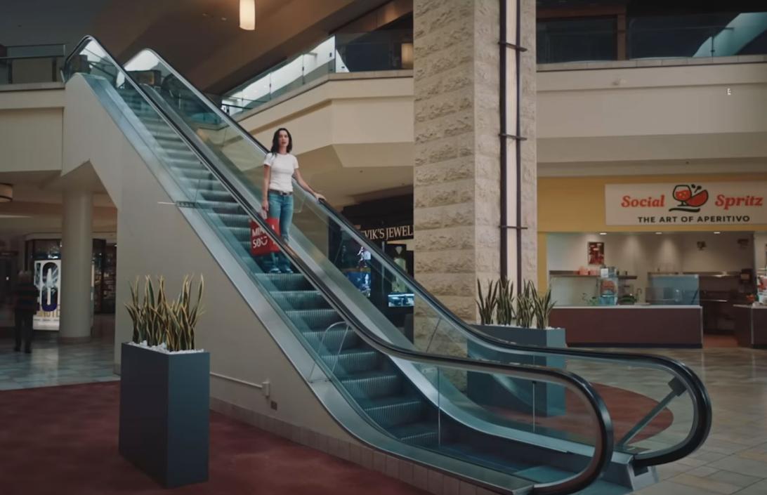 Кэти Перри спускается по эскалатору, держа красный пакет.