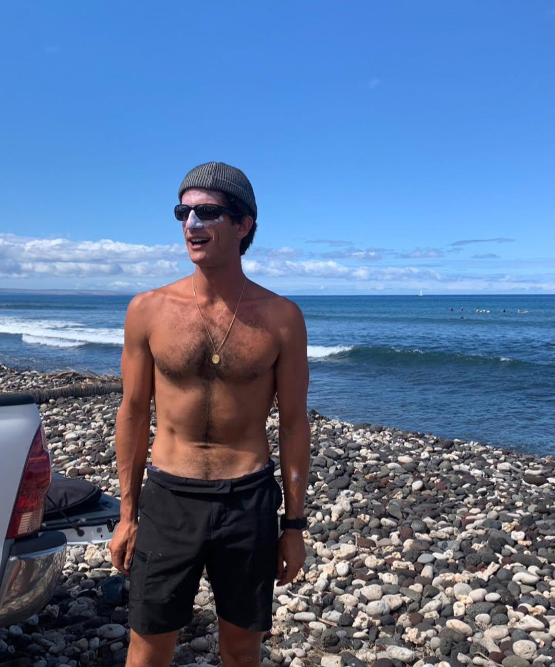 Джек Шлоссберг на пляже без рубашки, в шапке, солнцезащитных очках и с кремом от загара на лице.