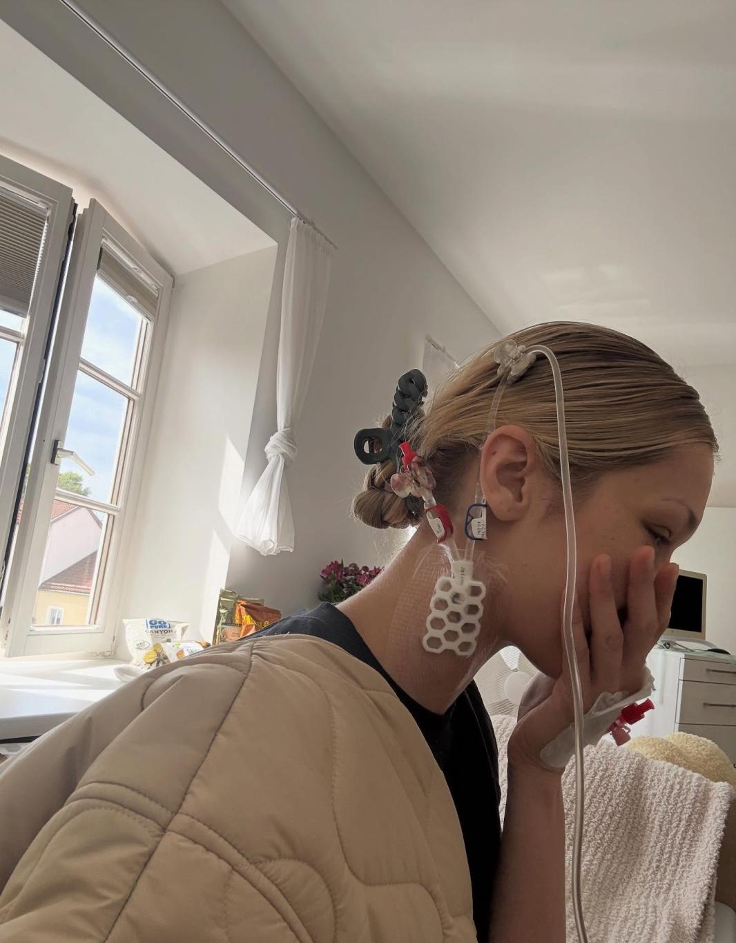 Белла Хадид на больничной койке, к шее и уху которой подведены медицинские трубки и аппараты.