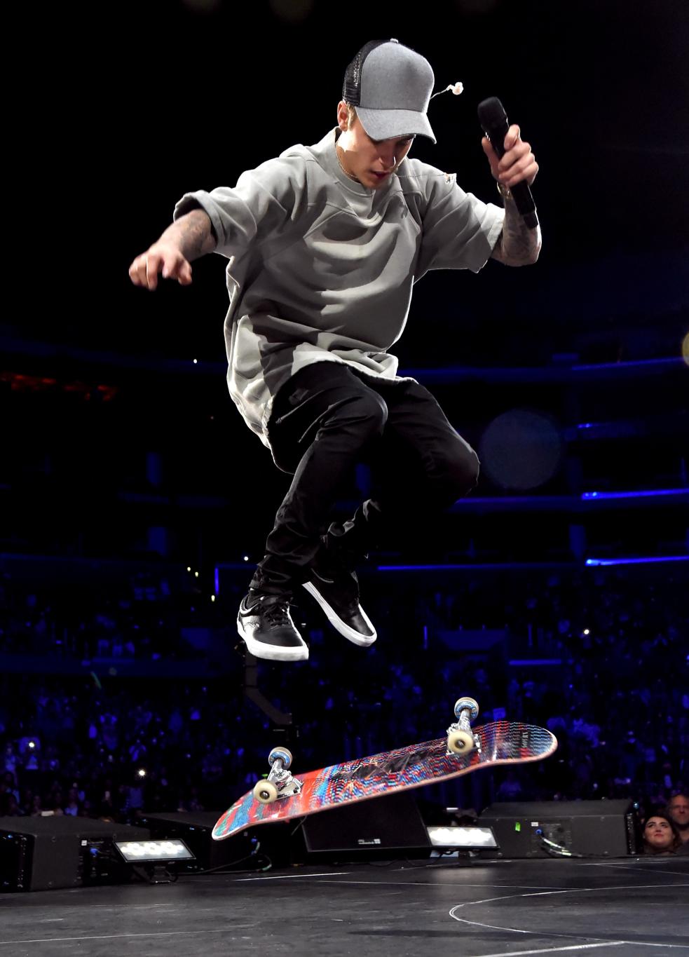 Джастин Бибер в полете на скейтборде, микрофон в руке.