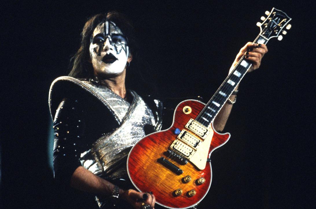 Эйс Фрейли из Kiss играет на гитаре в своем фирменном гриме и сверкающем темном костюме.