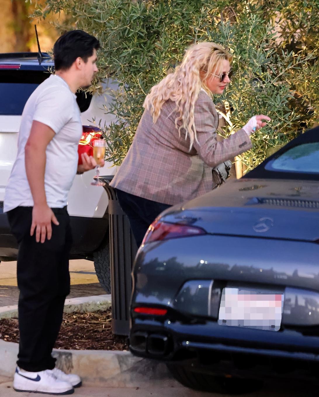 Бритни Спирс на фоне серого Мерседеса, а рядом сотрудник держит бокал шампанского.