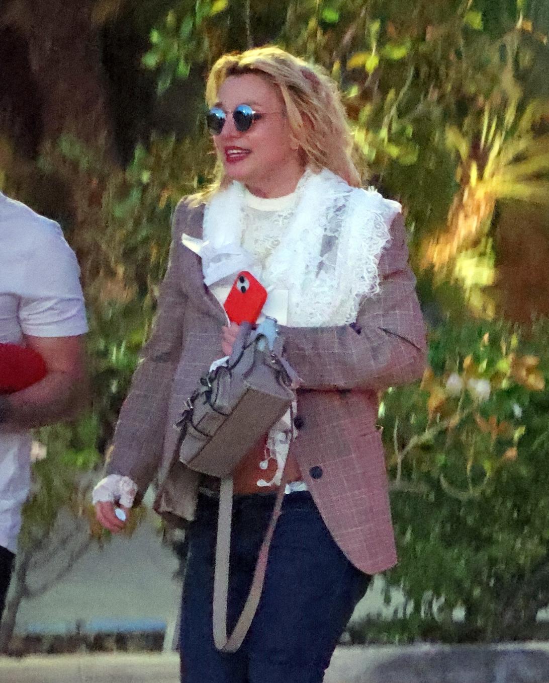 Бритни Спирс на улице: в зеркальных очках, серой клетчатой куртке, белом топе, джинсах, с серой сумкой и красным телефоном.