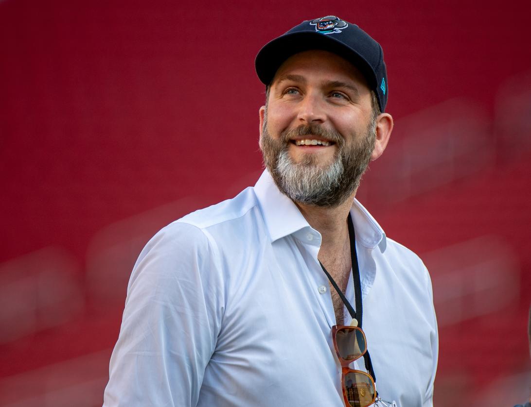 Хамфри Кер, исполнительный директор ФК «Рексем», улыбающийся, в бейсболке и белой рубашке.