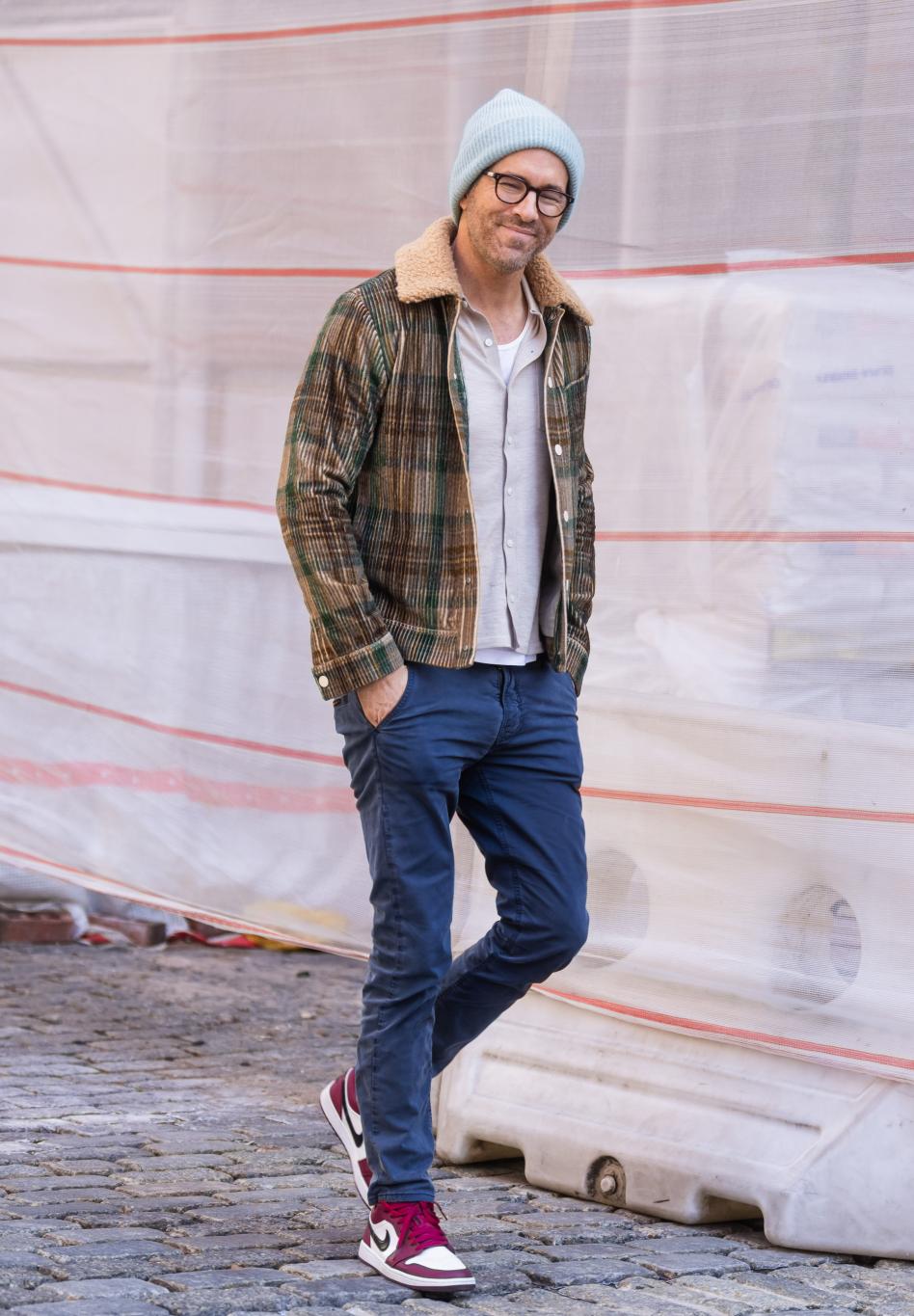 Райан Рейнольдс в светло-голубой шапке-бини, очках, клетчатой куртке и синих брюках.