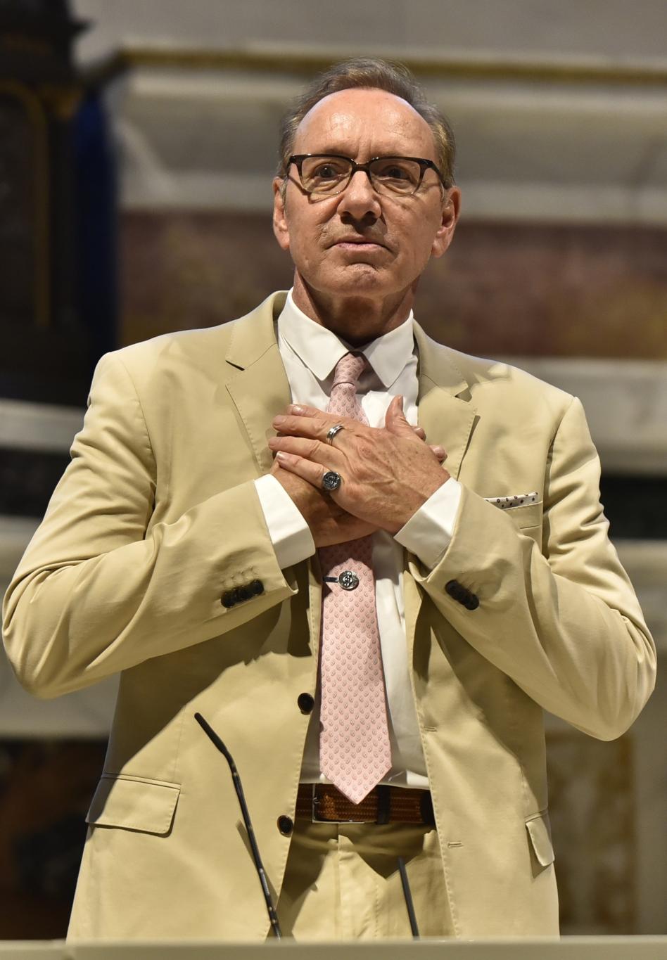 Актер Кевин Спейси предстал в бежевом костюме, розовом галстуке и очках, сложив руки на груди, на мастер-классе в церкви Сан-Франческо.