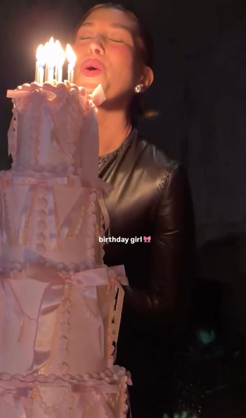 Хейли Бибер задувает свечи на высоком, изящном светло-розовом торте в свой день рождения.
