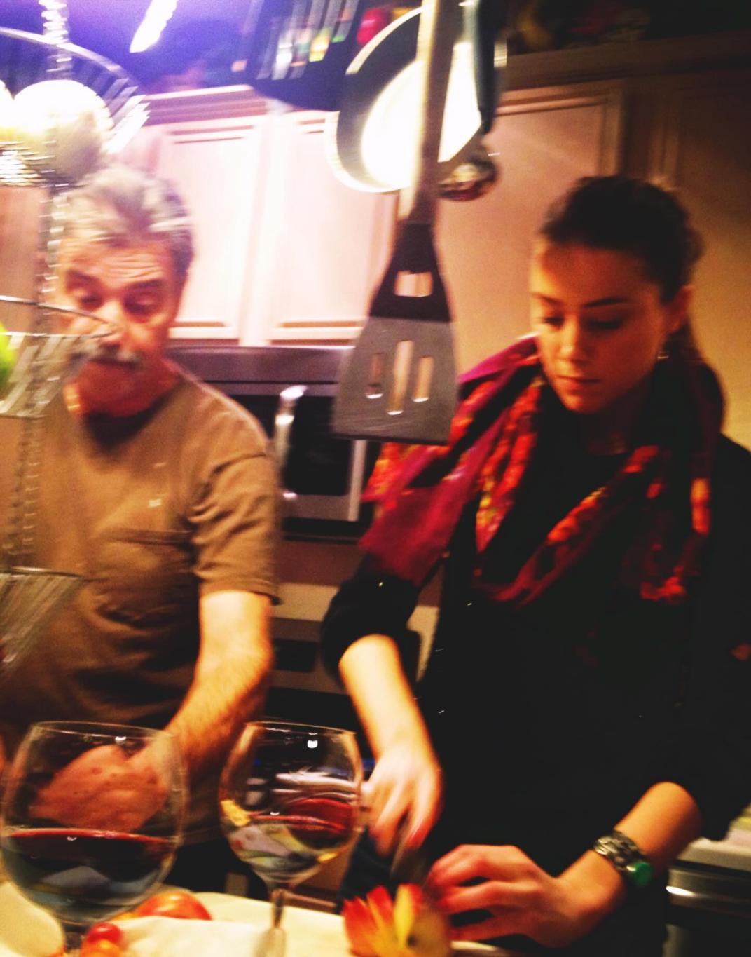 Эмбер Херд нарезает яблоко, мужчина стоит рядом; на столе два бокала красного вина.