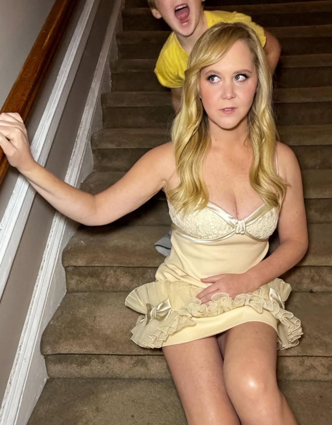 Эми Шумер в откровенном платье на лестнице. На заднем плане виднеется ребенок.