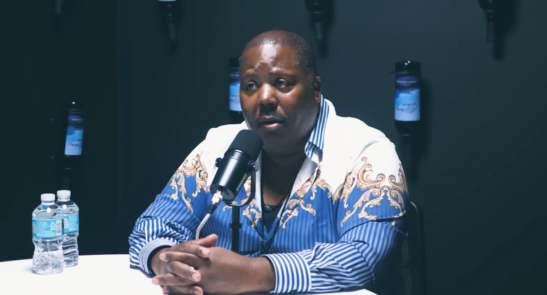 Мужчина в узорчатой рубашке говорит в микрофон.