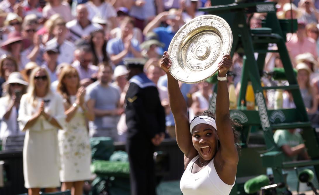Серена Уильямс поднимает над головой Уимблдонский трофей, празднуя триумф.