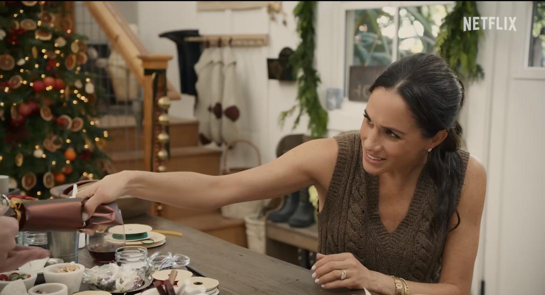 Меган Маркл с мужчиной разрывает рождественскую хлопушку, сидя за столом с творческими принадлежностями.