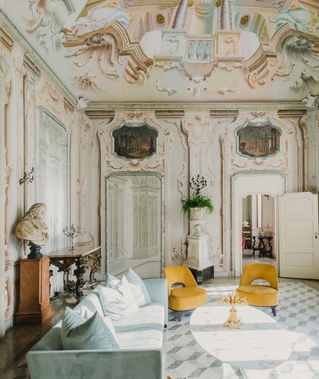 Основная гостиная Виллы Сола Кабиати отличается пышными фресками на стенах и потолках, светло-голубым диваном, двумя горчичными креслами и мраморным кофейным столиком.