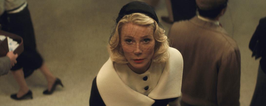 Гвинет Пэлтроу в образе: блондинка в черной шляпке с вуалью и элегантном бело-черном пальто, ее взгляд устремлен вверх.