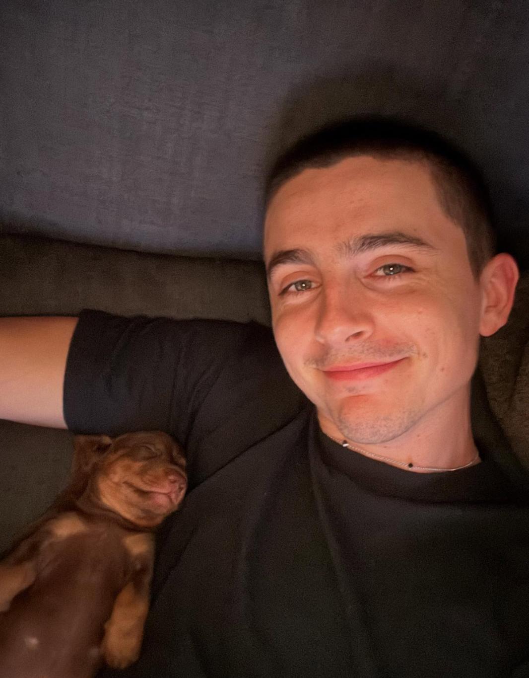 Тимоти Шаламе улыбается, делая селфи со спящим коричневым щенком на груди.