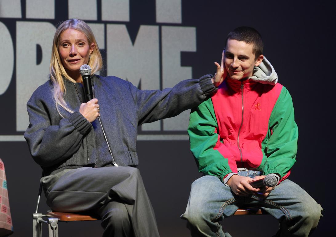 Гвинет Пэлтроу держит микрофон левой рукой, касаясь Тимоти Шаламе.