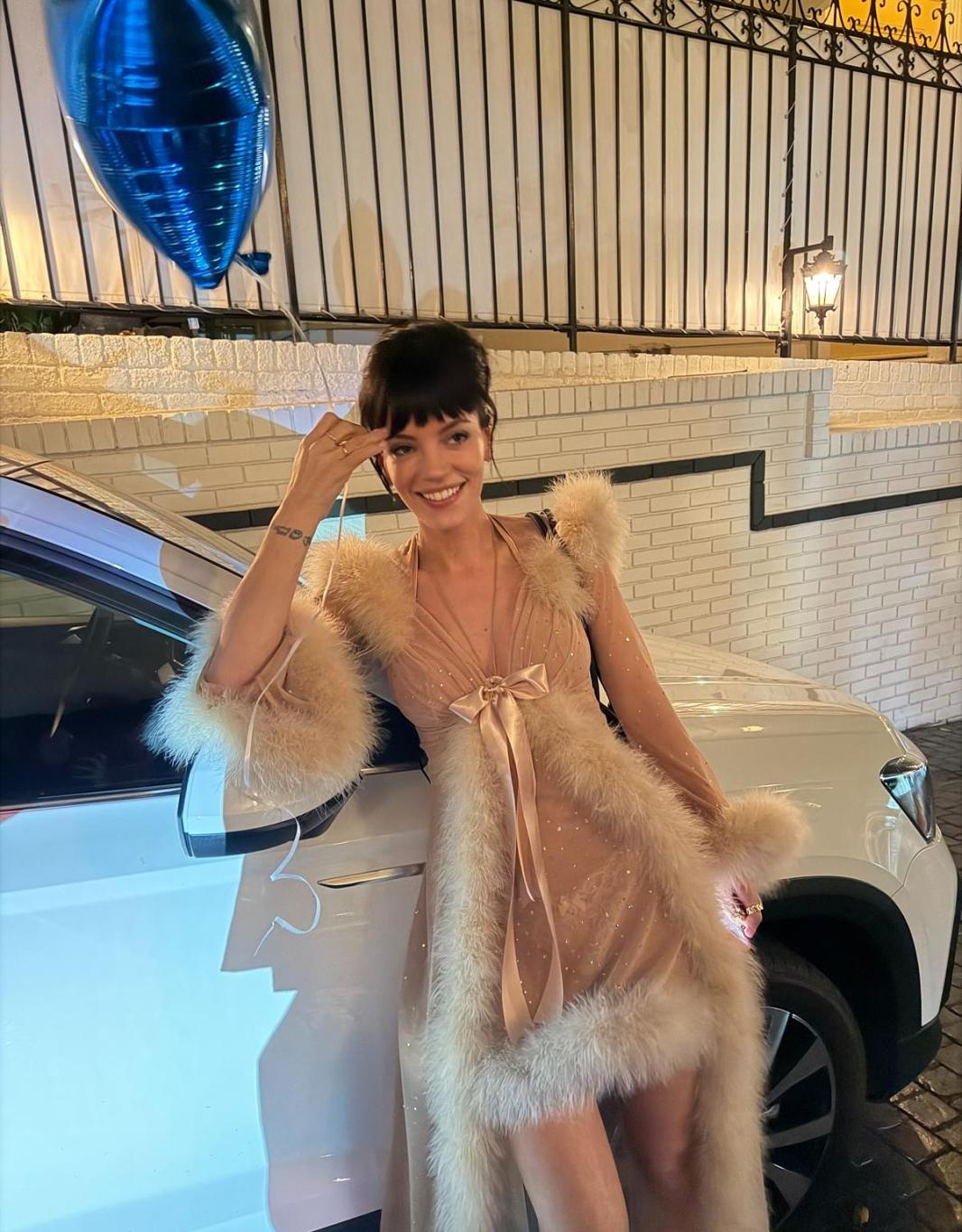 Лили Аллен в смелом полупрозрачном платье, украшенном перьями, у белой машины.