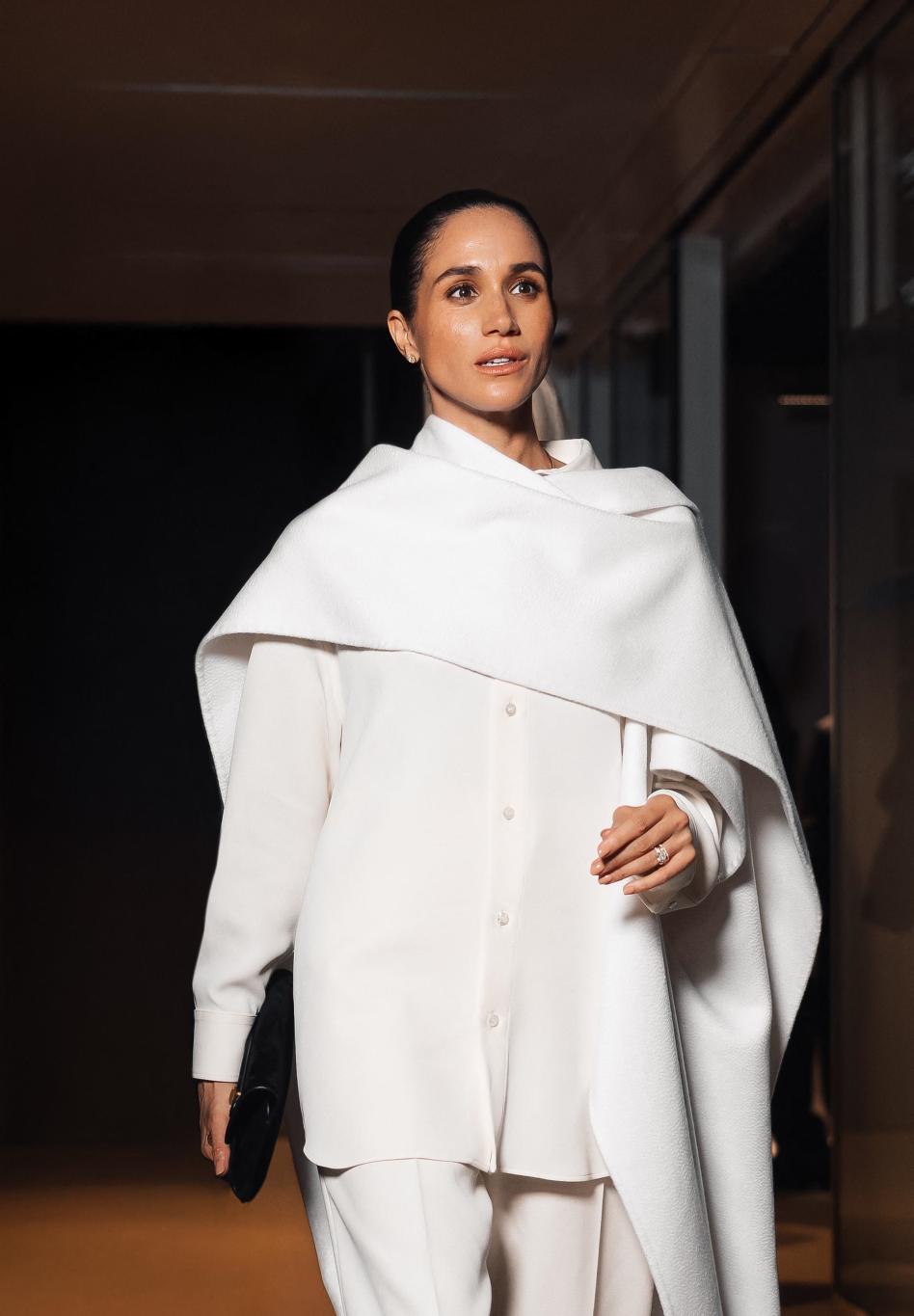 Меган Маркл в элегантном кремовом брючном костюме, с шалью в тон и чёрным клатчем.