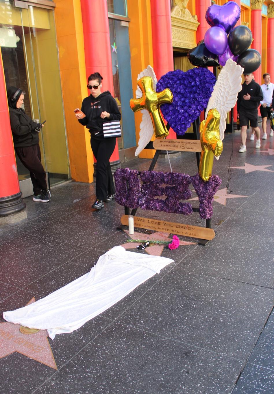 Посвящение Оззи Осборну на Голливудской Аллее славы: фиолетовые цветы, шары и плакат от Шэрон с детьми.