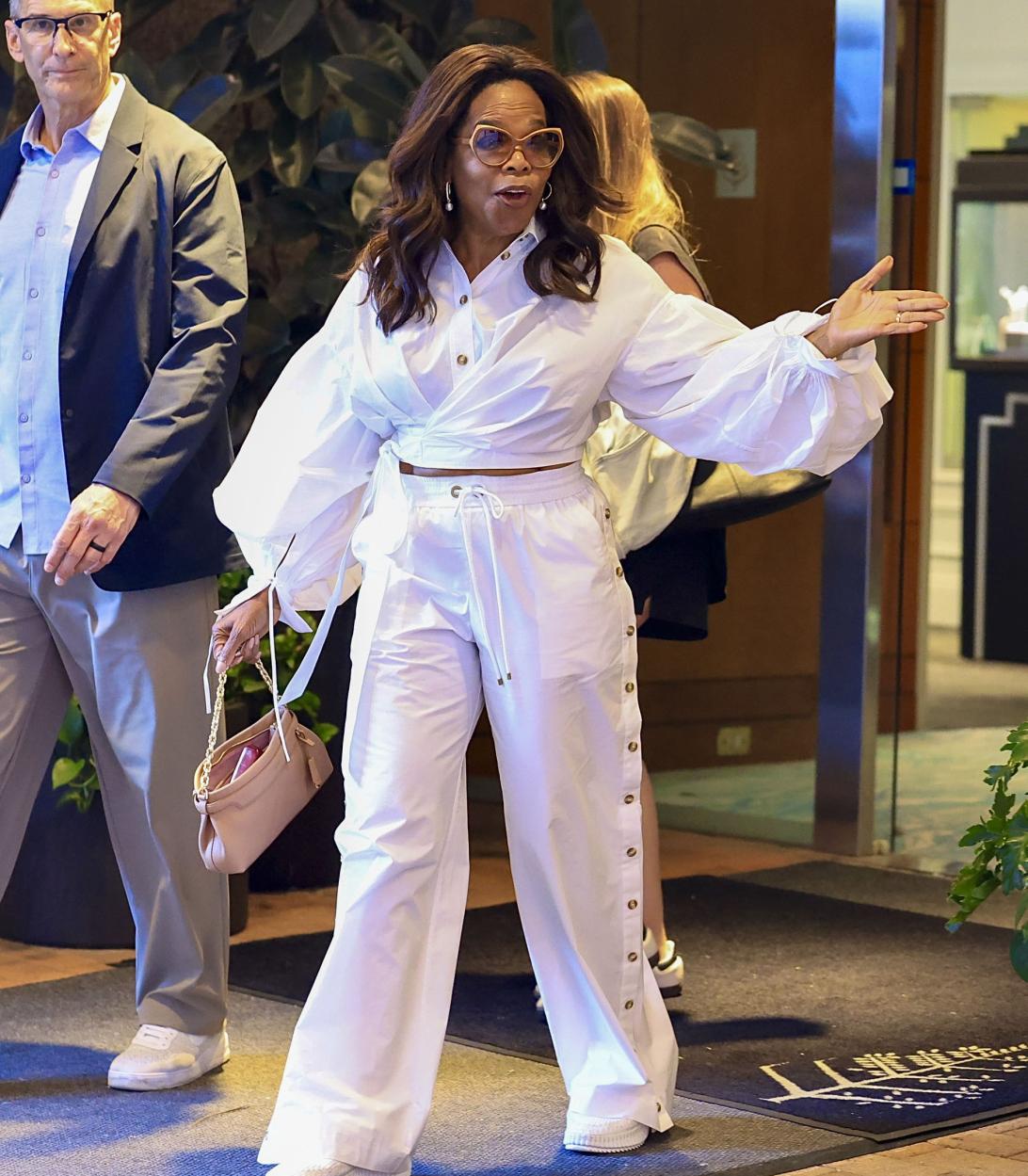 Опра Уинфри в белом ансамбле: укороченный топ с рукавами-фонариками и широкие брюки с высокой талией, на кнопках, с тканевым поясом.