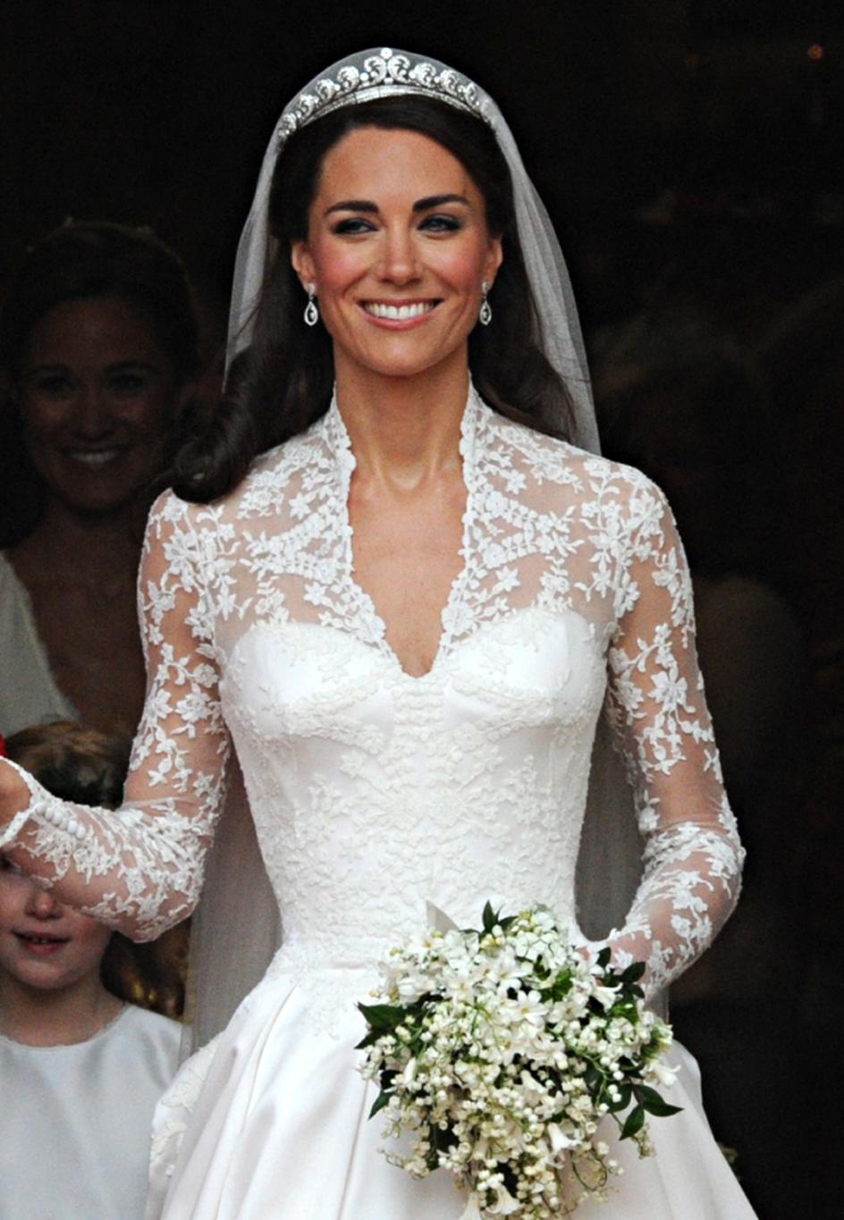 Герцогиня Кембриджская Кейт в свадебном платье с улыбкой держит букет ландышей.