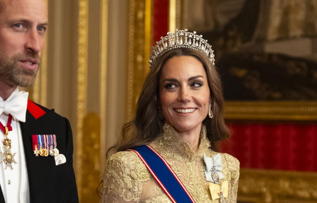 Принцесса Уэльская Кэтрин, в диадеме, парадном платье и орденской ленте, улыбается рядом с принцем Уильямом.