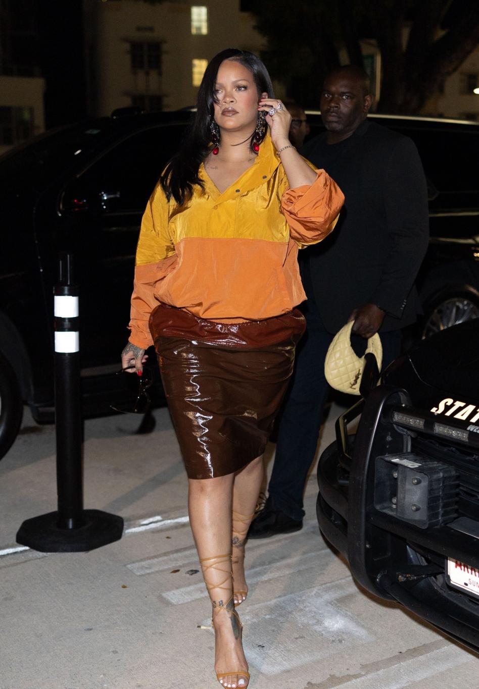 Рианна в оранжевом топе и коричневой юбке, держит темные солнцезащитные очки.