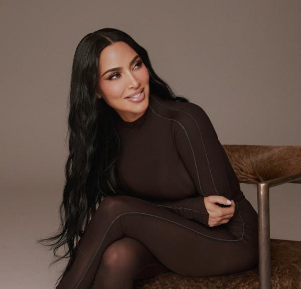 Ким Кардашьян в темно-коричневом боди сидит на пушистом коричневом кресле.