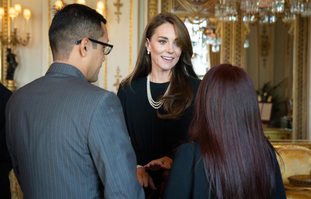 Принцесса Кейт Миддлтон улыбается, общаясь с двумя людьми.