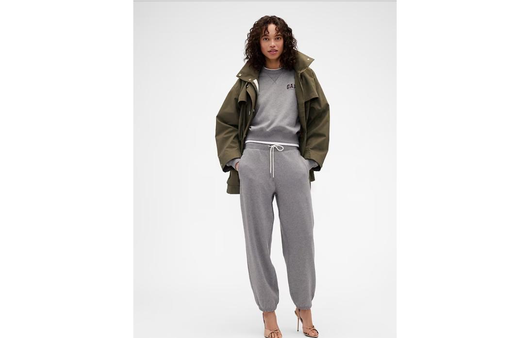 Стильная девушка в худи Gap, зеленой куртке, серых штанах и бежевых босоножках.