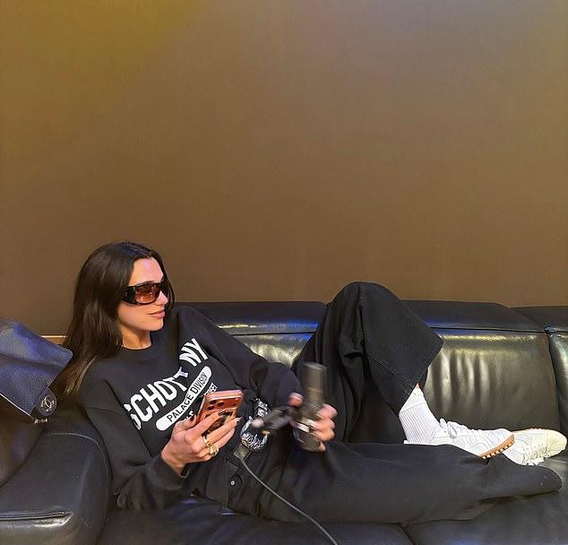 Дуа, в наряде для студии, с микрофоном в руке, уютно расположилась на кожаном диване, готовясь к записи.