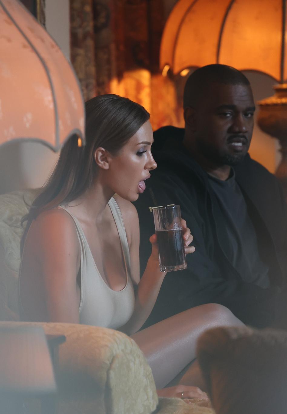 Бьянка Ценсори пьет из бокала рядом с Канье Уэстом в полумраке.