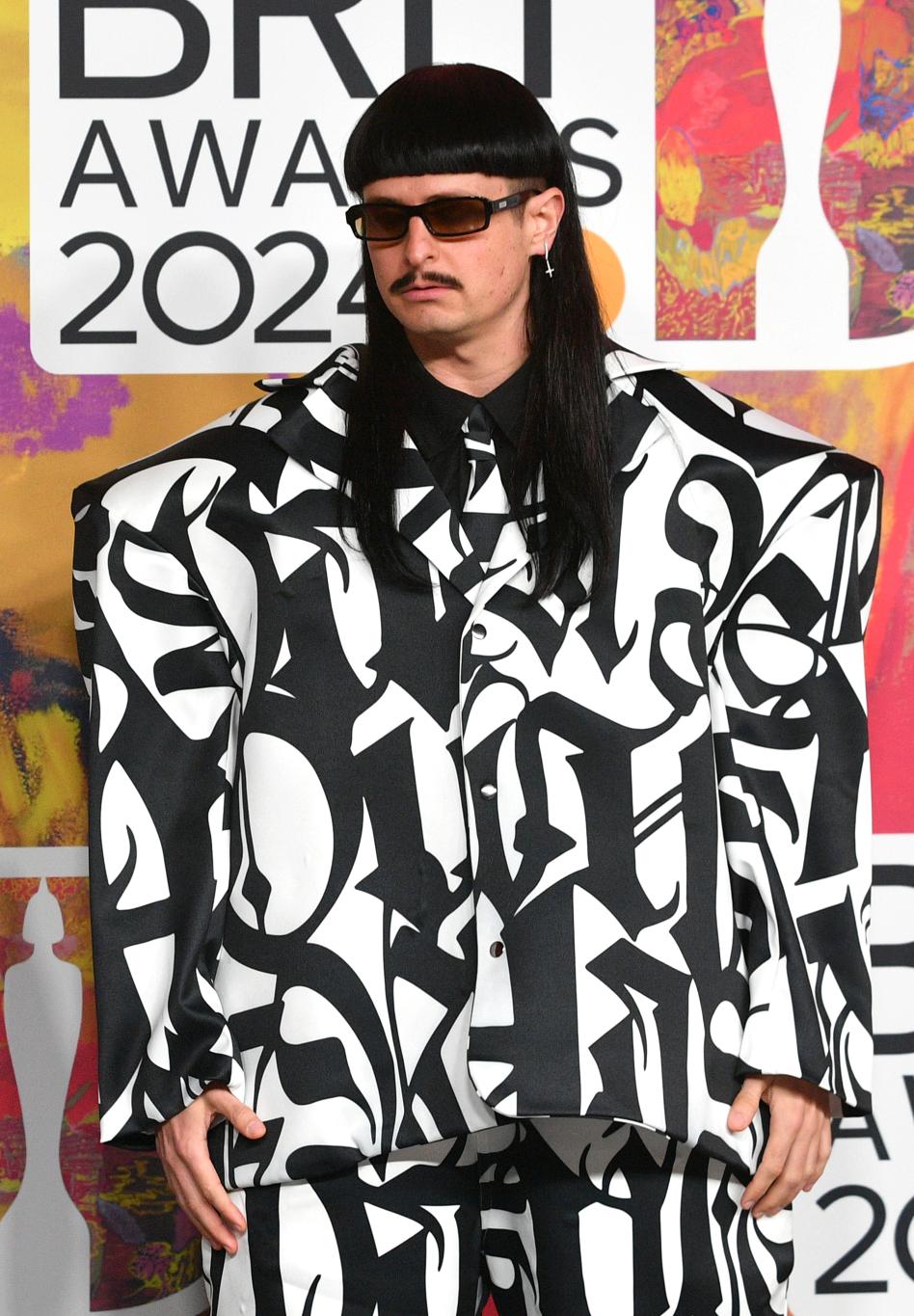 Оливер Три в черно-белом костюме, темных очках и с усами на церемонии BRIT Awards.