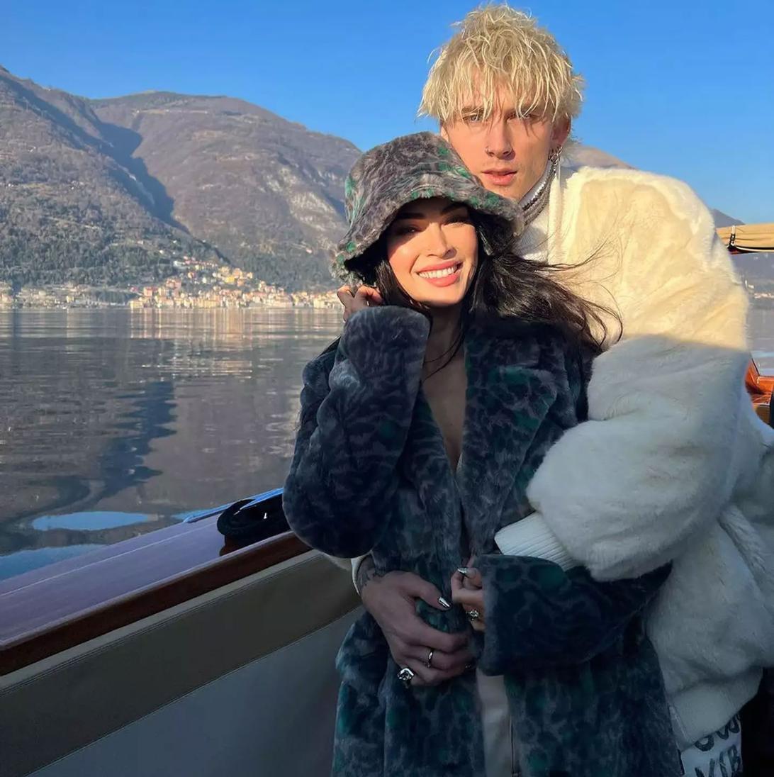 Machine Gun Kelly обнимает Меган Фокс на лодке, на фоне гор и озера.