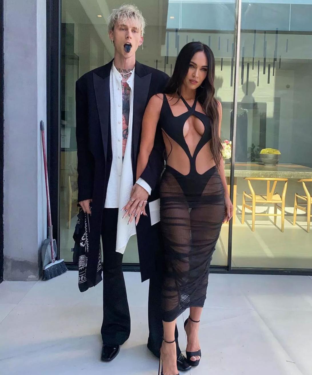 Меган Фокс и Machine Gun Kelly держатся за руки перед стеклянной дверью.